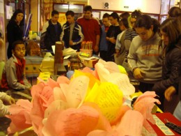 Foto de las flores libro de Mayte Gómez en primer término con estudiantes visitando la exposición